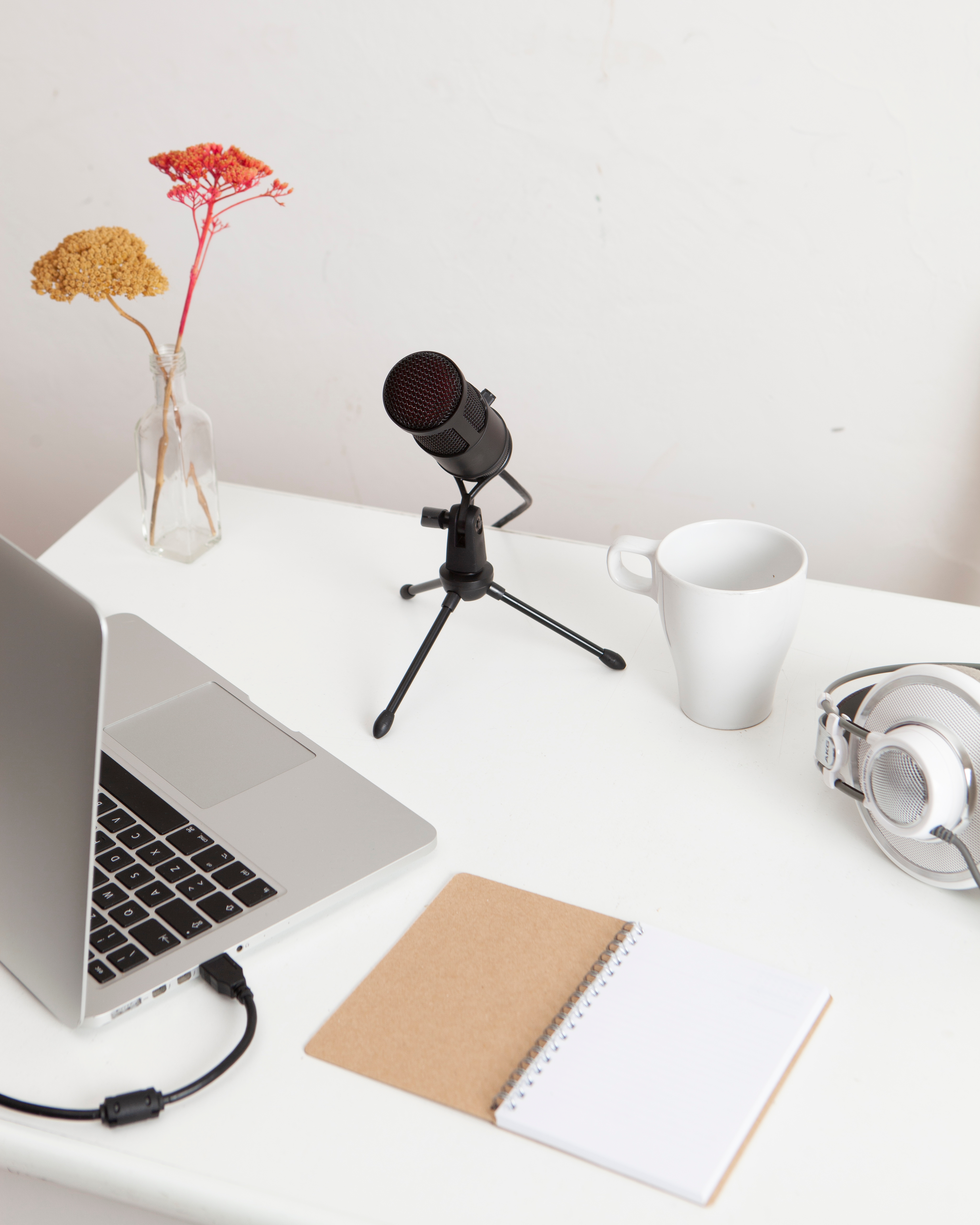 A microphone, laptop, notebook, mug and headphones on a desk.